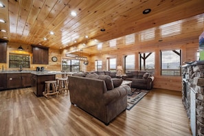 Ein geräumiges Blockhaus-Interieur mit Holzbalkendecke, einer Küchenzeile, einem Wohnbereich mit Sofas und großen Fenstern mit Aussicht.