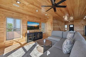 A wooden cabin interior with a sofa, TV, and ceiling fan. - Mountain Spirits (Sevierville)