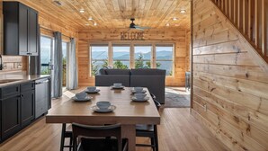 Een houten interieur met een eettafel gedekt voor vier personen, een bank en een uitzicht op bergen door grote ramen.
