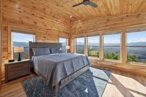 Ein Schlafzimmer einer Holzhütte mit einem Bett, Nachttischen und großen Fenstern mit Blick auf die Berge.
