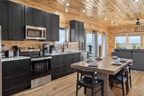 A modern kitchen with dark cabinets, stainless steel appliances, and a wooden ceiling. - Mountain Spirits (Sevierville)