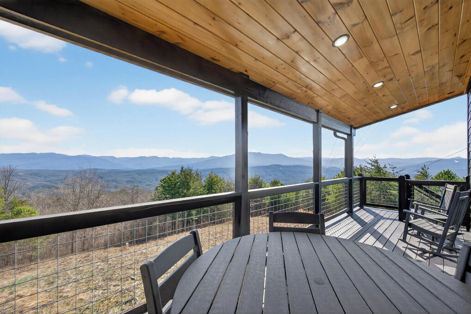 A wooden deck with a table and chairs, overlooking a mountainous landscape.