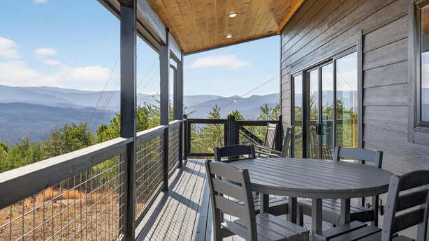 Een houten terras met een tafel en stoelen, met uitzicht op een bergachtig landschap.
