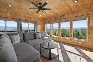 A modern log cabin interior with a sectional sofa, a round coffee table, and a 'WELCOME' sign. - Mountain Spirits (Sevierville)