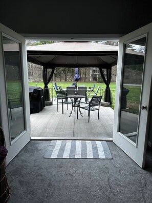 Ein überdachter Patio-Bereich mit Tisch und Stühlen, einem Grill und Blick auf eine Rasenfläche.