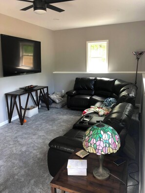 Ein Wohnzimmer mit einer schwarzen Ledersofa, einem Flachbildfernseher, einem Couchtisch aus Holz, einer Tiffany-Lampe und einem Fenster mit Tageslicht.
