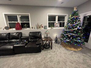 Ein Wohnzimmer mit einem Ledersofa, einem Weihnachtsbaum und einem Fenster mit Dekorationen.