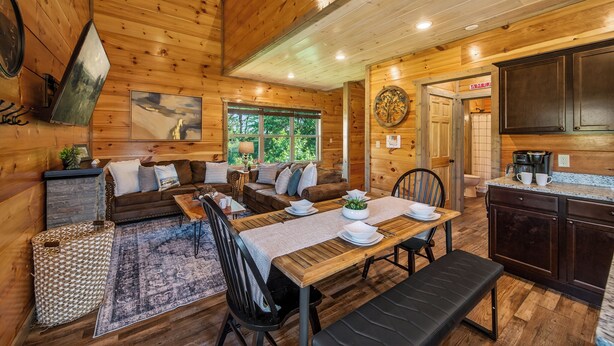 A cozy cabin interior with a wooden dining area, a sofa, and a kitchen with dark cabinets. - New! Indoor Pool, Game Room, Families Welcome! (Sevierville)