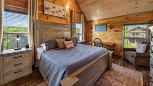 A wooden cabin bedroom with a bed, a desk, a chair, and a window with a view. - New! Indoor Pool, Game Room, Families Welcome! (Sevierville)