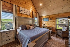 A wooden cabin bedroom with a bed, a desk, a chair, and a window with a view. - New! Indoor Pool, Game Room, Families Welcome! (Sevierville)