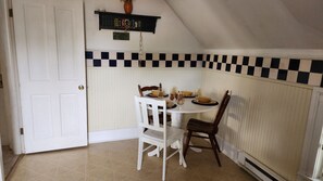 A dining area with a white table, two chairs, a checkered wall, and a door.