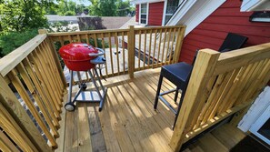 A wooden deck with a red grill, a chair, and a house in the background.