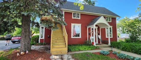 A red house with a porch, a wooden staircase, and a flag.