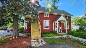 A red house with a porch, a wooden staircase, and a flag.
