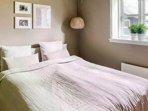 Une chambre à coucher avec un lit, des oreillers, une lampe fixée au mur et des œuvres d’art encadrées.