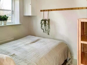 Ein Schlafzimmer mit einem Bett, einer Holzablage, einem Fenster mit Pflanzen und einer hängenden Pflanze.