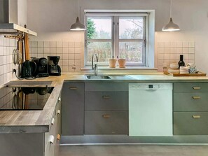 Une cuisine moderne équipée d’un lave-vaisselle, d’un évier à deux bacs et d’une fenêtre donnant sur un espace verdoyant.