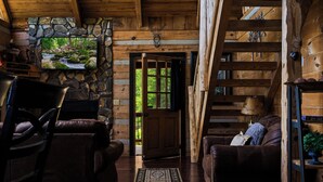 A log cabin interior with a stone fireplace, leather furniture, and a view of the outdoors. - A-Frame Mountain Retreat | Jaw-Dropping Smoky Mountain Views, Hot Tub & Arcade (Pigeon Forge)