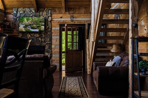 L’intérieur d’une cabane en rondins, avec une cheminée en pierre, des meubles en cuir et une vue sur l’extérieur.