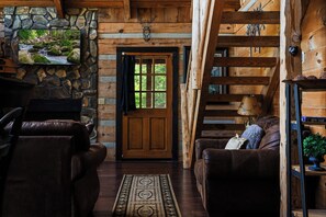 L’intérieur d’une cabane en rondins, avec une cheminée en pierre, des murs en bois, une porte en bois, des meubles en cuir et une vue sur l’extérieur.
