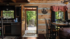 A wooden interior with a kitchen, dining area, and a view of the outdoors. - A-Frame Mountain Retreat | Jaw-Dropping Smoky Mountain Views, Hot Tub & Arcade (Pigeon Forge)