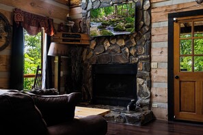 Ein gemütliches Blockhaus-Interieur mit Kamin aus Stein, einem an der Wand montierten Fernseher und einer Holztür.