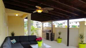 A covered outdoor seating area with a sofa, a grill, and potted plants. - Spacious & Bright 5-bedroom house just a short walk to the beach! (Oistins)