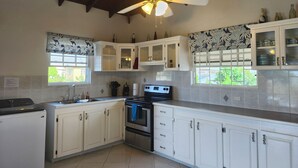 A kitchen with white cabinets, a stove, a ceiling fan, and a window with a view. - Spacious & Bright 5-bedroom house just a short walk to the beach! (Oistins)