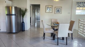 A modern kitchen with a stainless steel refrigerator, a dining area with a glass table and chairs, and a ceiling fan. - Spacious & Bright 5-bedroom house just a short walk to the beach! (Oistins)
