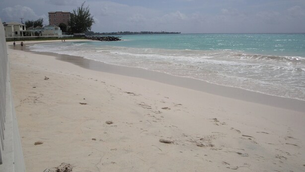 A beach with a sandy shore, a few footprints, and a building in the background. - Spacious & Bright 5-bedroom house just a short walk to the beach! (Oistins)