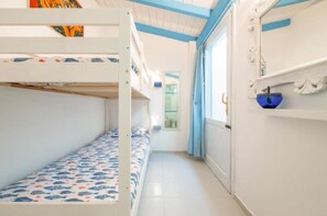 A bunk bed room with a patterned bedspread, a blue bowl on a shelf, and a window with curtains.