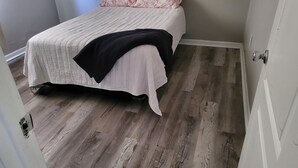 A bedroom with a bed, a door, and a wooden floor.