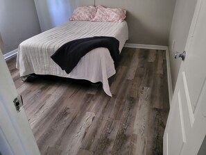 A bedroom with a bed, a door, and a wooden floor.