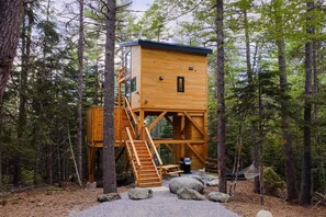 Una cabaña de madera con escaleras, una ventana y una mesa de picnic en un bosque.