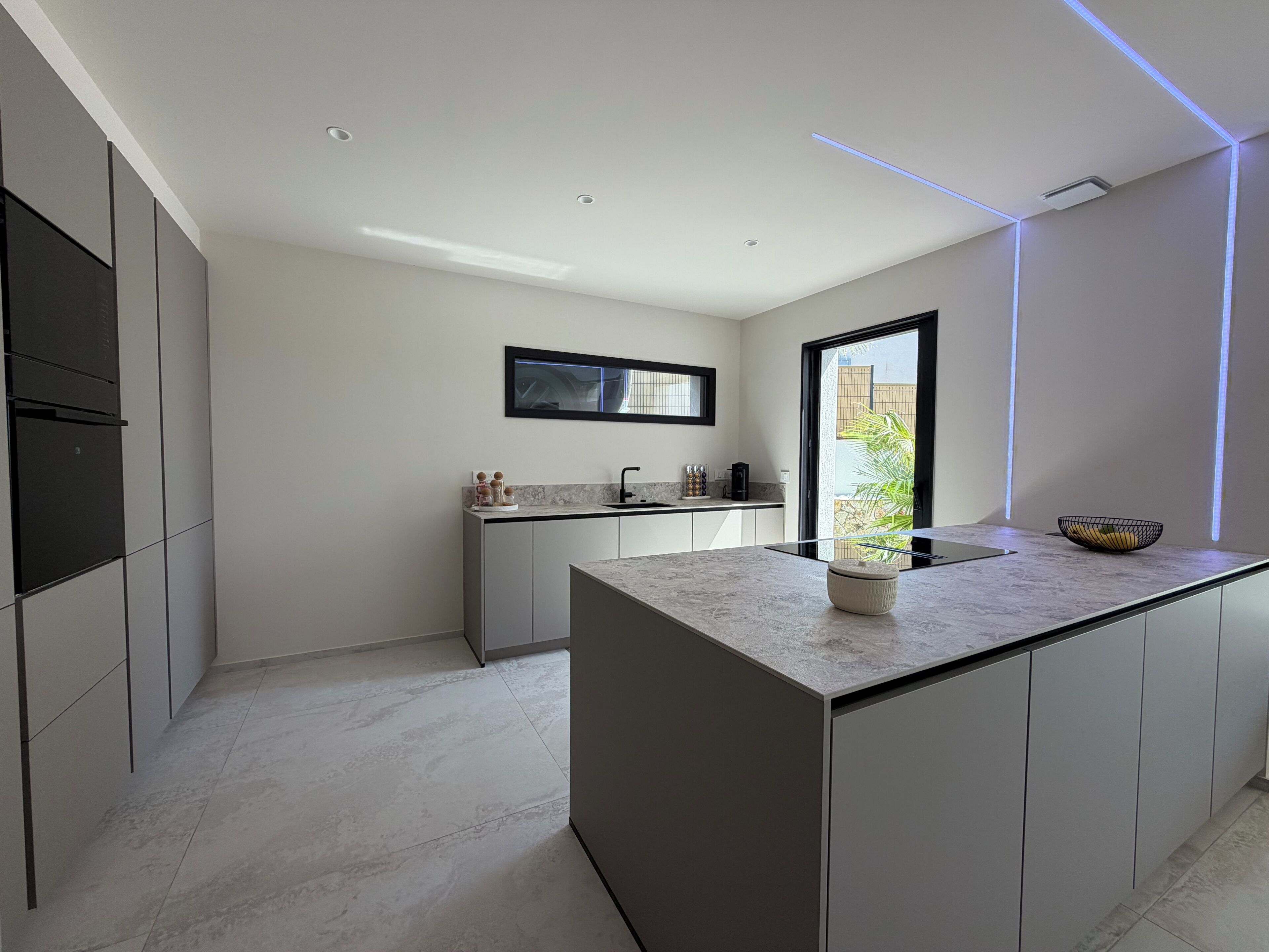 A modern kitchen with a central island, built-in appliances, and a large window.