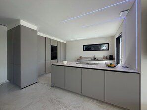 A modern kitchen with a large island, built-in appliances, and a flat-screen TV mounted on the wall. - Villa Lamartine with heated pool, 10 minutes from the beach and downtown—BRAND-NEW … (Provence-Alpes-Côte d'Azur)