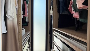Un vestidor con ropa colgada y doblada, estanterías de madera y una puerta corredera.