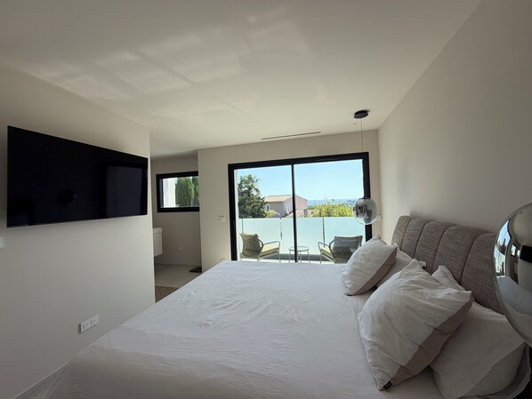 A bedroom with a bed, a TV mounted on the wall, and a view of the outside through a sliding door. - Villa Lamartine, 10 minutes from the beach and downtown—BRAND-NEW … (Provence-Alpes-Côte d'Azur)