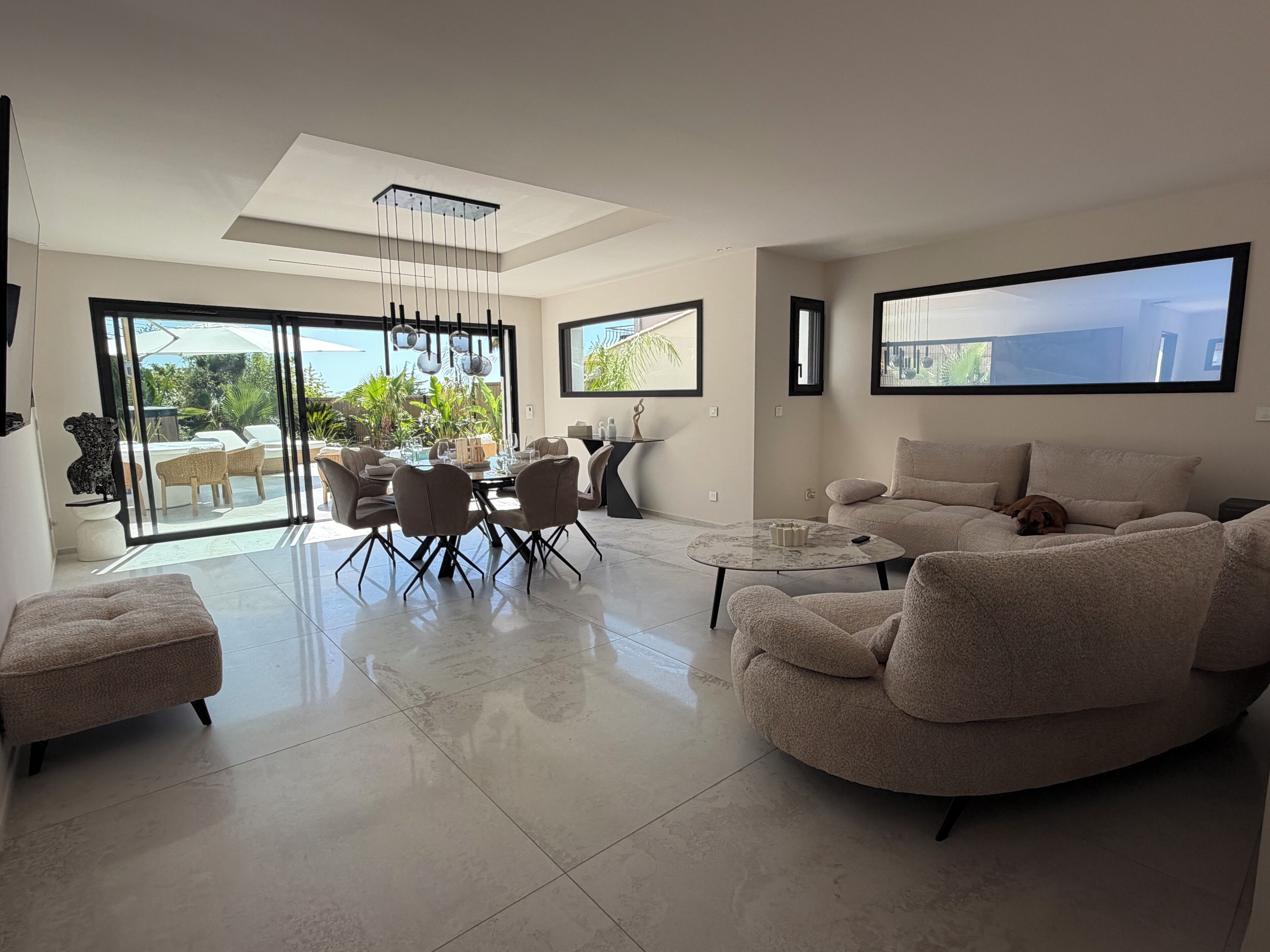 A modern living room with a dining area, large windows, and a view of the outdoors.