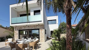 Una casa moderna de dos pisos con un patio, mobiliario exterior y un muro de piedra.