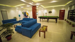Un vestíbulo de hotel con sofás azules, una mesa de billar y plantas en macetas.