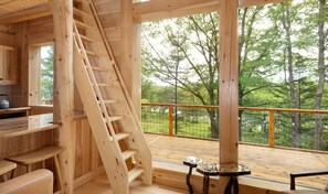 A wooden interior with a staircase, a kitchen area, and a deck with a view of trees.
