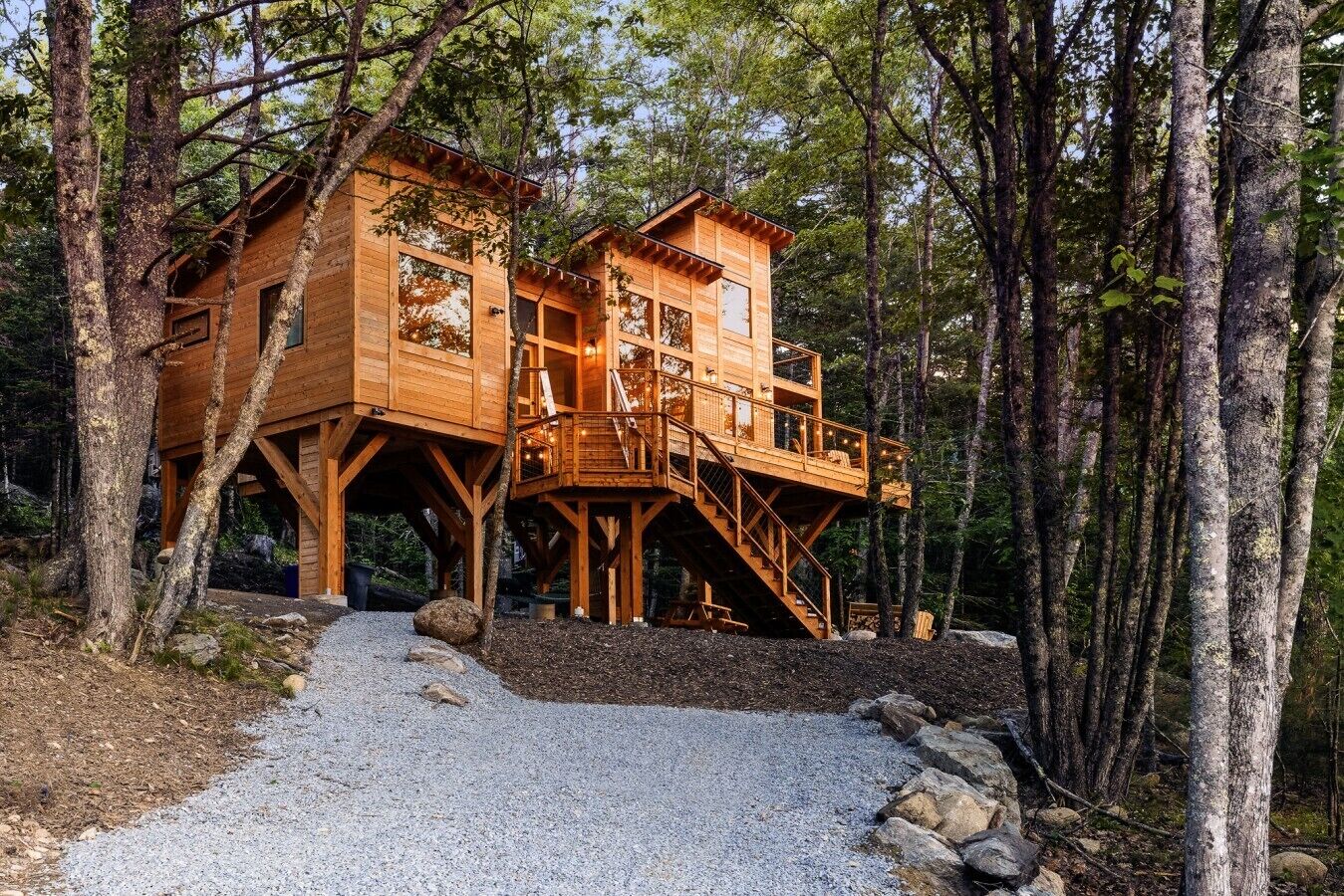 Una cabaña de madera con terraza y escalera, rodeada de árboles.