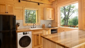 Una cucina moderna con mobili in legno, una lavatrice integrata e un'ampia finestra con vista sugli alberi.