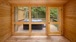 Una baita di legno con una porta vetrata che dà su un patio esterno con idromassaggio.