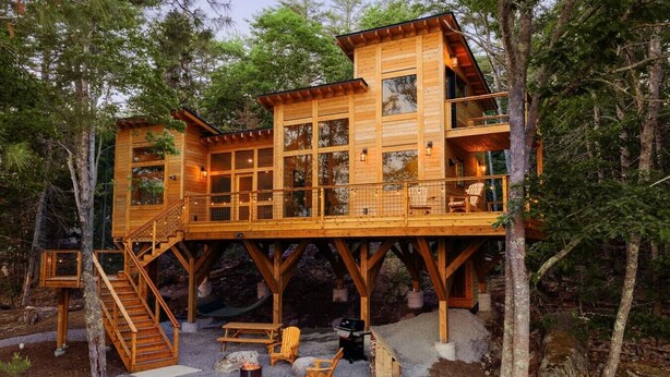 Una baita in legno a più piani con veranda, posti a sedere all'aperto e un braciere.