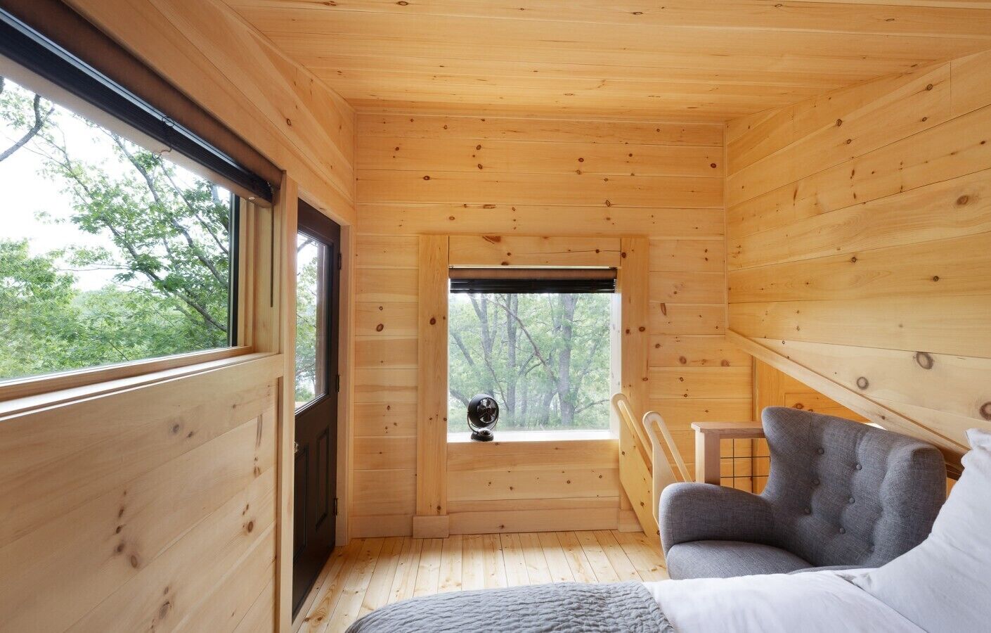 Ein Holzblockhaus-Interieur mit einer Couch, einem Fenster mit Blick auf Bäume und einer Tür.