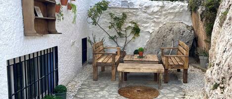 A patio with wooden furniture, potted plants, and a textured wall.
