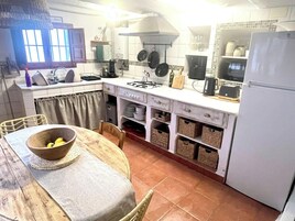 Una cocina con una mesa de comedor, sillas, un refrigerador y diversos electrodomésticos.