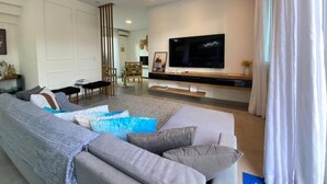 Una sala de estar moderna con un televisor de pantalla plana grande, un sofá seccional gris y una zona de comedor con una mesa alta y sillas.